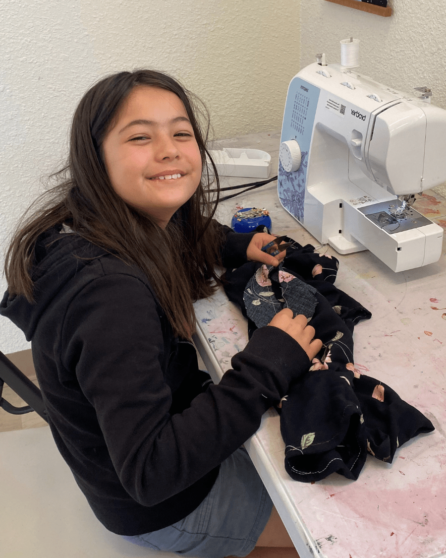 smiling camper sewing a floral shirt with a sewing machine